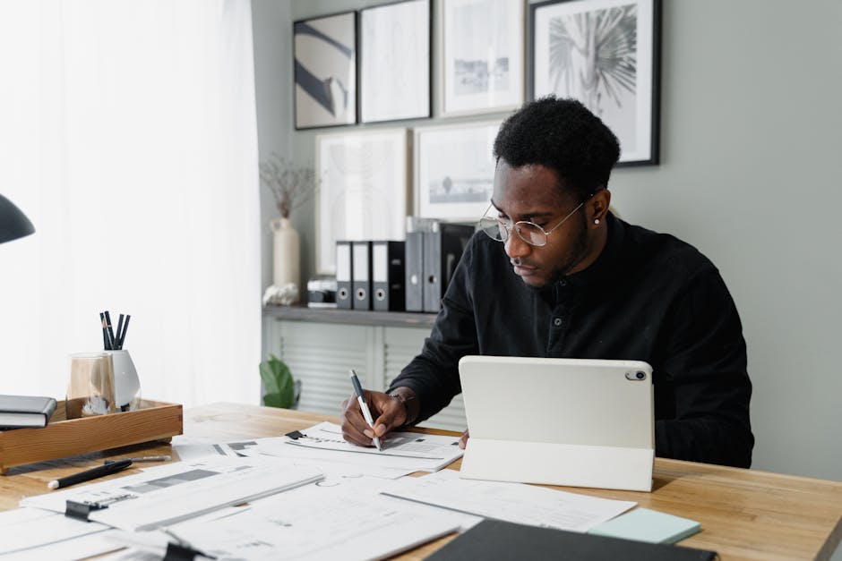 A professional man engaged in writing and using a tablet at a modern office desk.