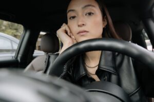 Close-up of an Asian woman sitting inside a car, appearing thoughtful and serene, with hand on her face.