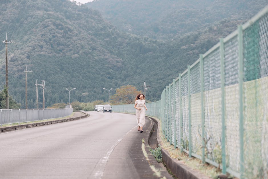 A woman jogging on a mountain road next to a fence with scenic views.