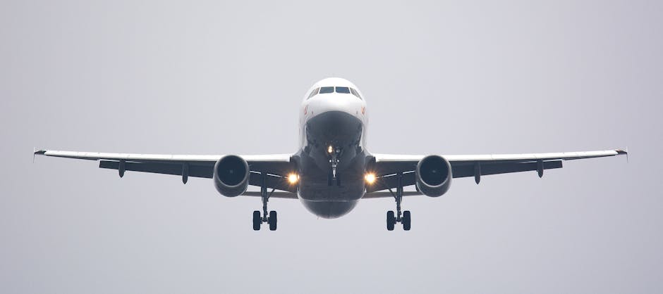 A commercial airliner captured head-on, preparing to land against a cloudy sky.