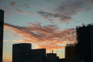 Silhouette of city buildings against a vibrant sunset sky with clouds.