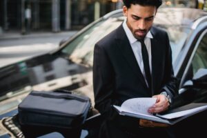 Confident businessman reviewing documents on the street beside a car.