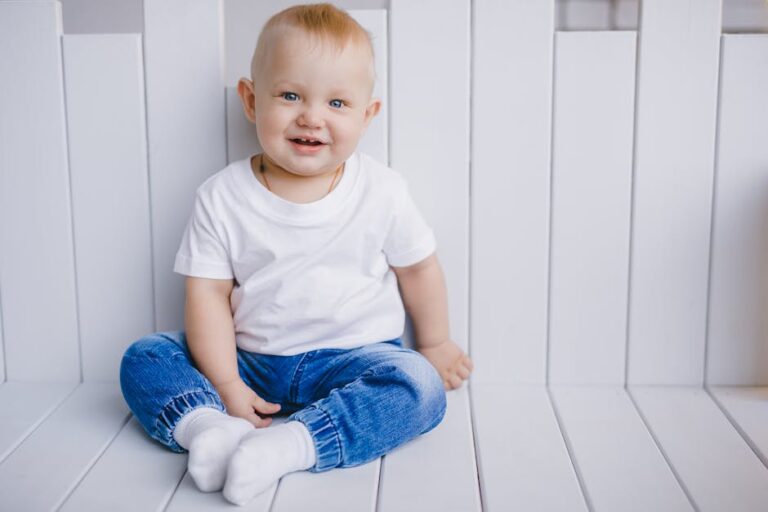 Charming portrait of a smiling baby boy in a white t-shirt and blue jeans, sitting indoors.