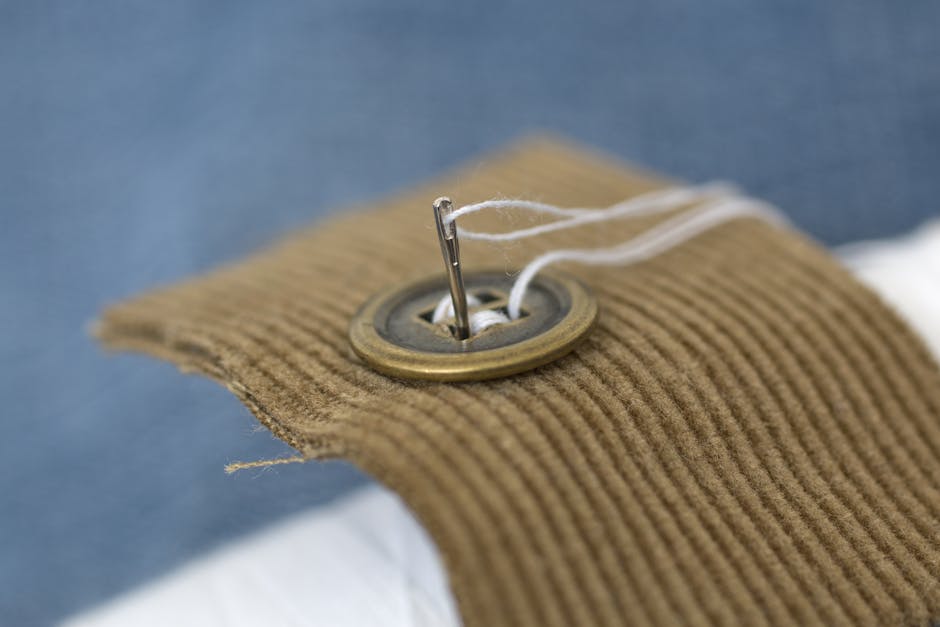 A detailed view of a needle threading a button on corduroy fabric.