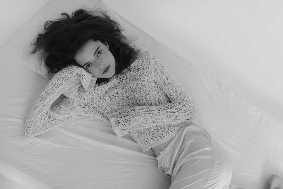 Black and white portrait of a woman in a lace top lying on a bed, exuding elegance.