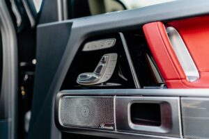 Close-up of modern luxury car door featuring red leather seats and metal trim controls.