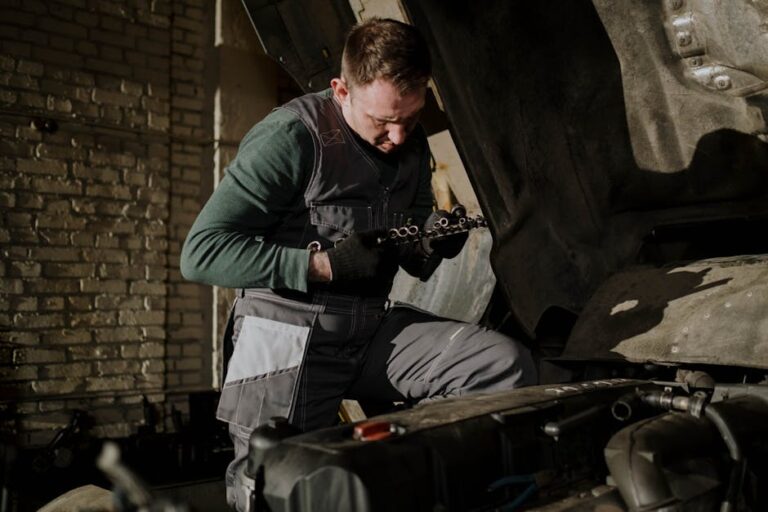 A car mechanic in overalls inspects the engine parts inside a garage to ensure proper functioning.