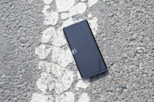 A cracked smartphone lying on a textured asphalt road surface captured from above.