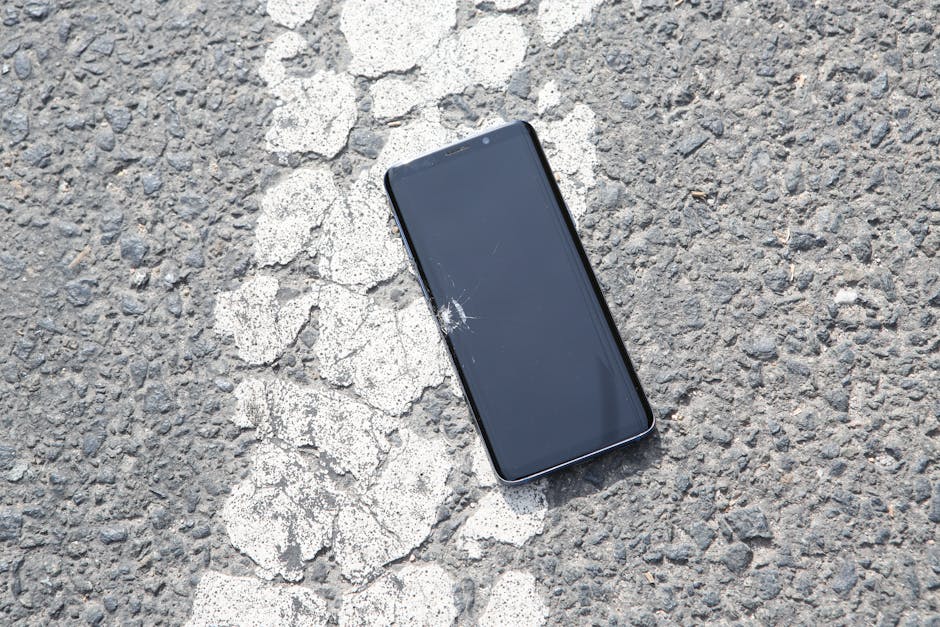 A cracked smartphone lying on a textured asphalt road surface captured from above.