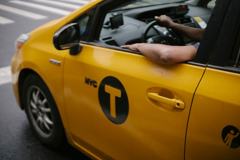 Close-up of a yellow NYC taxi with driver's arm resting on the window, captured in an urban setting.