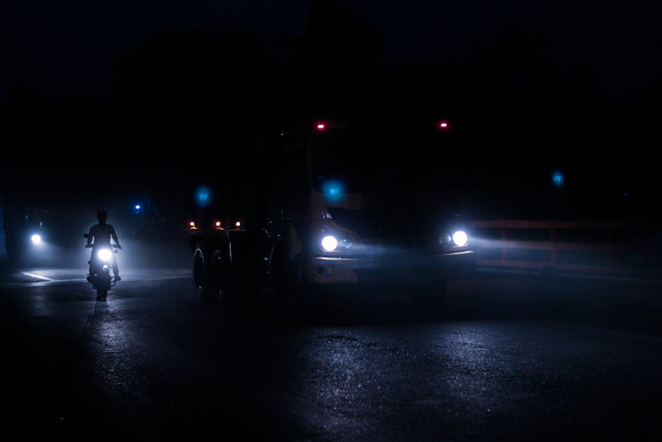 A striking night scene featuring a motorbike and truck with bright headlights on a foggy road.