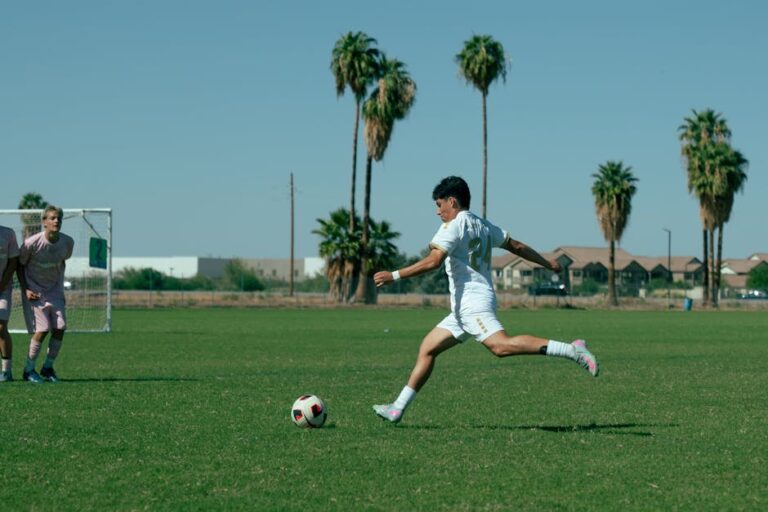A soccer player in motion kicking a ball on a sunny day outdoors.