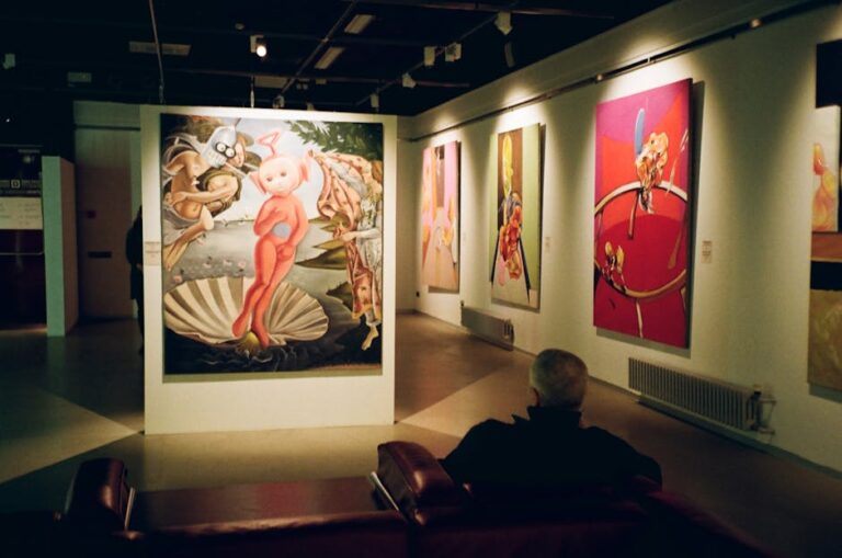 Person seated in a contemporary art museum observing vibrant paintings on display, creating an immersive cultural experience.