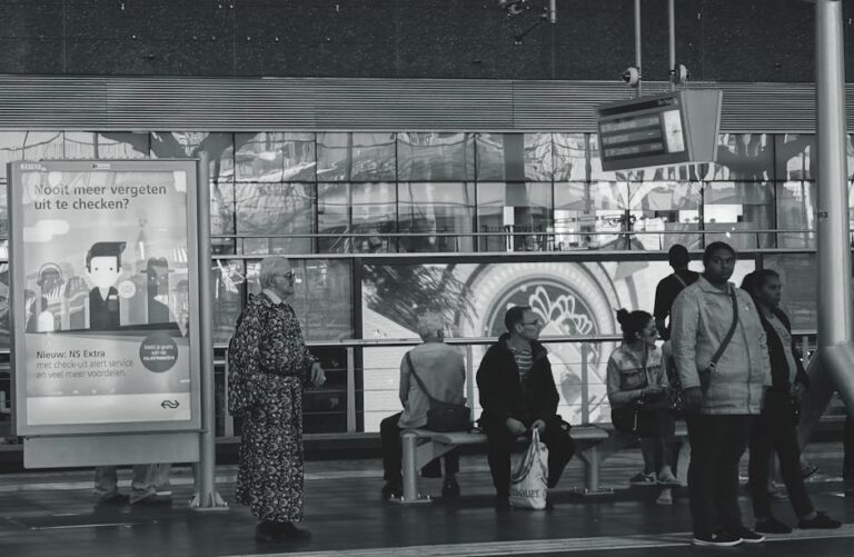 Black and white image of people waiting at a railway station, capturing daily travel life.
