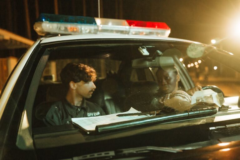 Two police officers in a patrol car during the night, engaging in a conversation.