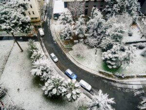 Aerial shot of a snow-covered road with cars and trees in an urban area during winter.