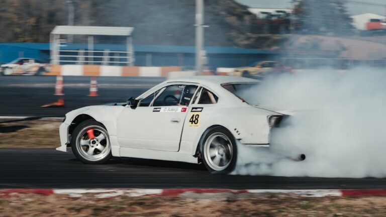 White car performing a thrilling drift maneuver on a motor racing track, emitting smoke.